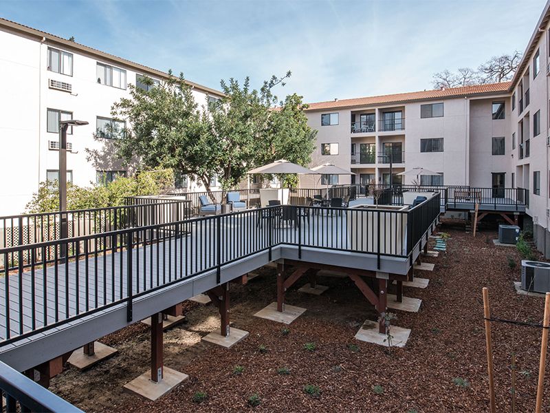 An outdoor view of an apartment complex with balconies and a landscaped area featuring trees.