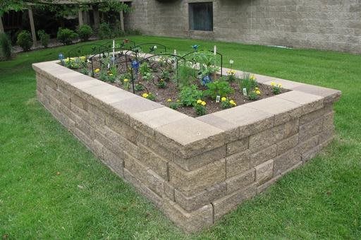 A raised garden bed constructed with stone walls, featuring various plants and vegetables.