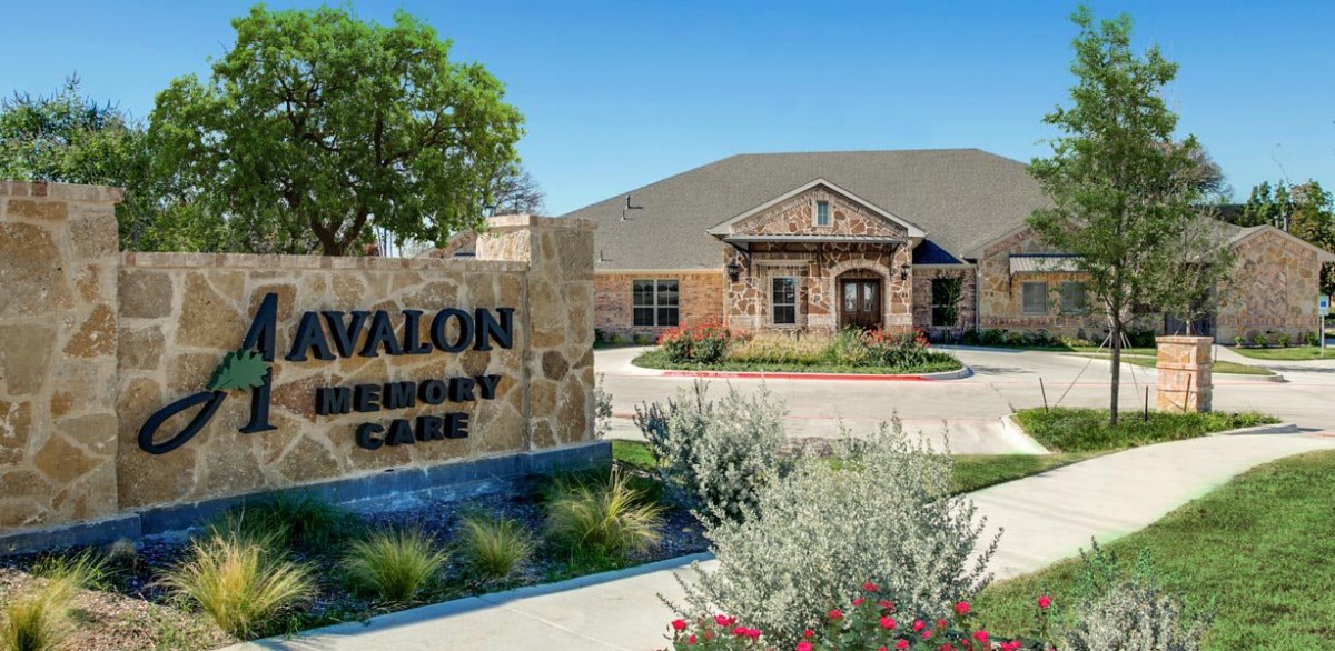 An entrance to a facility with a sign and landscaped surroundings.