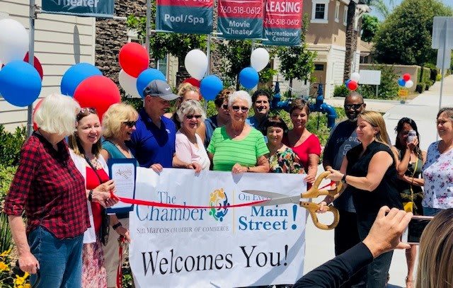 A community ribbon-cutting event with a group of people holding a banner and balloons.
