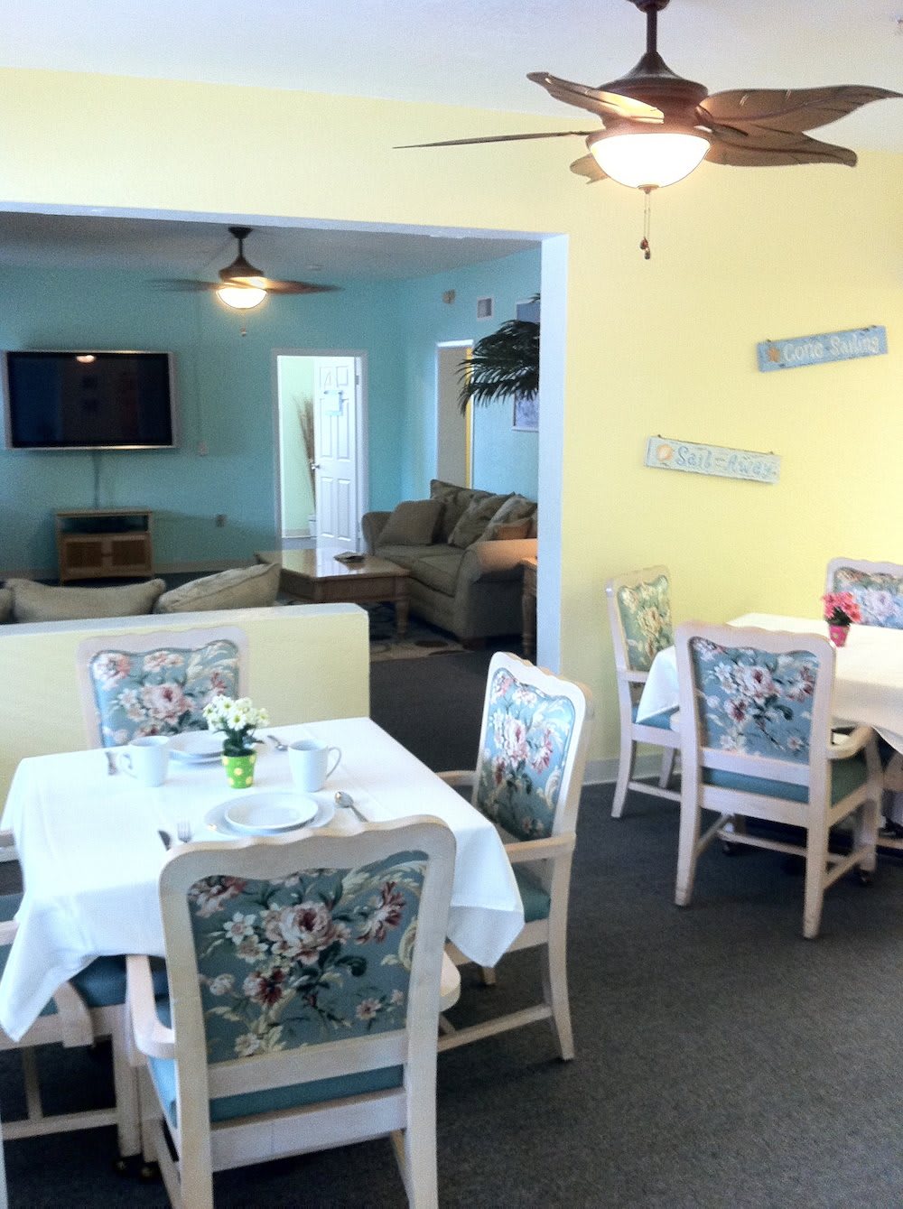 A cozy dining area with tables and chairs, adjacent to a living room featuring a sofa and television.