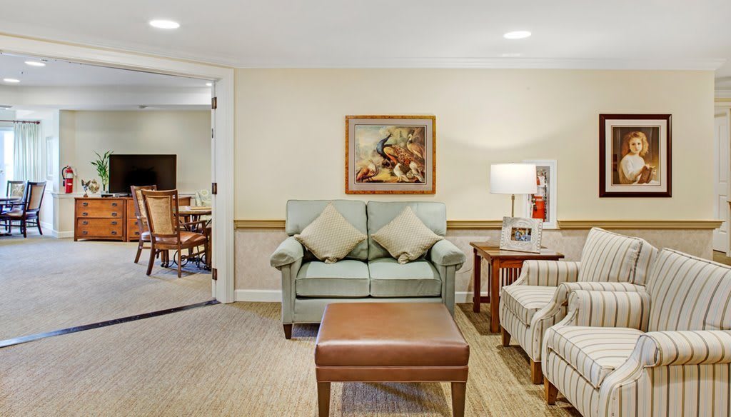 A cozy living room with a sofa, armchair, and a painting on the wall.