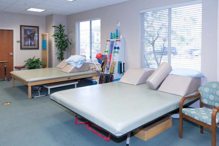 A clean and organized physical therapy treatment room equipped with various exercise tools and beds.
