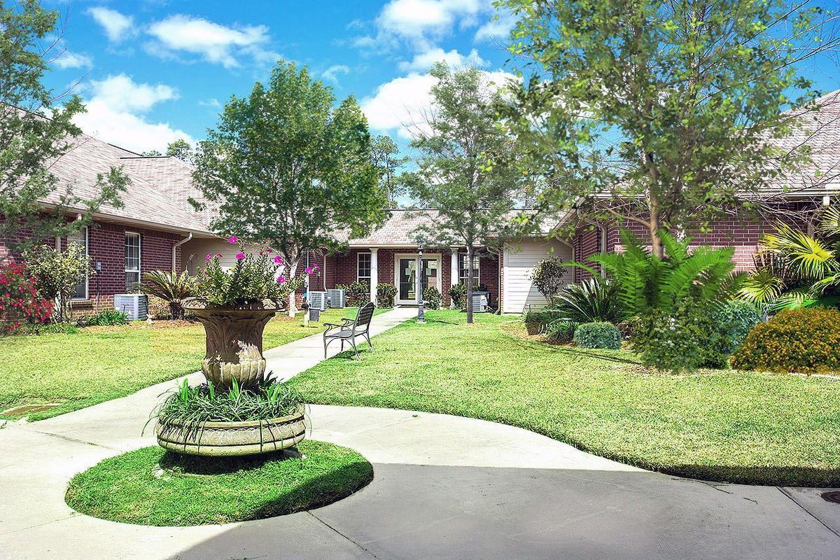 A scenic outdoor garden with a pathway, bench, and surrounding trees leading to a building.