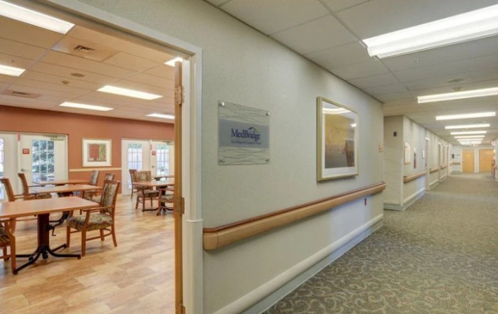 A view of a hallway in a nursing home facility with an open doorway leading to a dining area.
