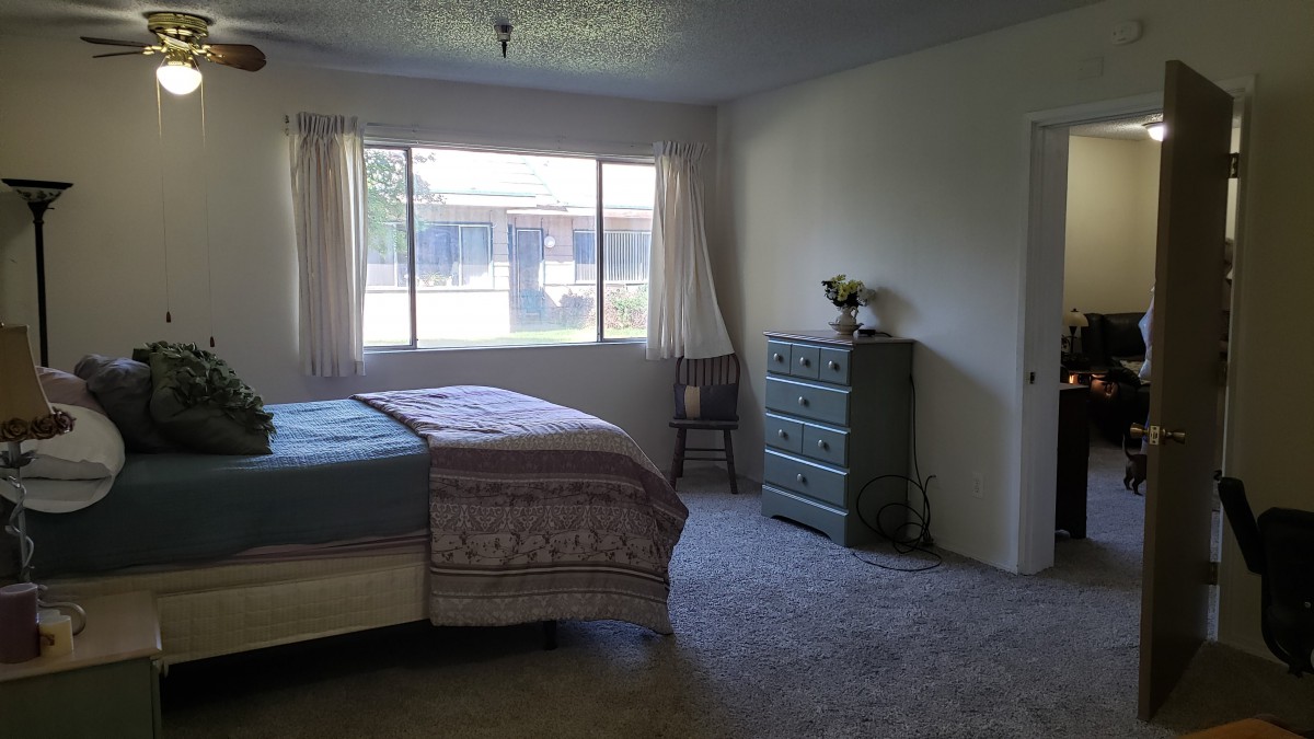 A cozy bedroom with a large window, a bed, and a dresser.