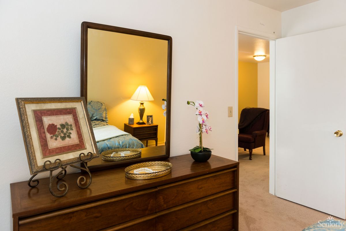 A cozy bedroom featuring a wooden dresser with a mirror and decorative items.