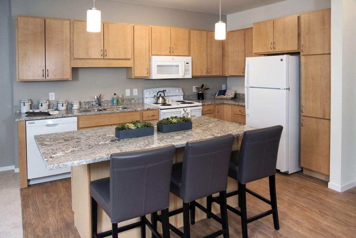 A modern kitchen with a central island and seating, featuring wooden cabinets and appliances.