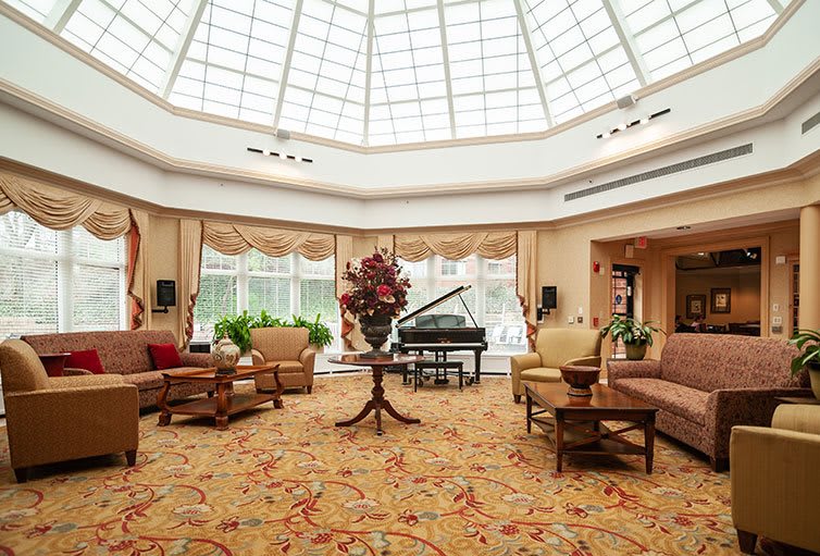Spacious lounge with elegant furniture and a grand piano under a large skylight.