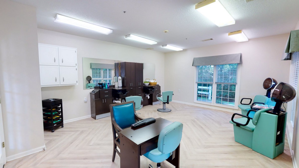 A modern hair salon interior with chairs and a desk, featuring large windows and ample lighting.