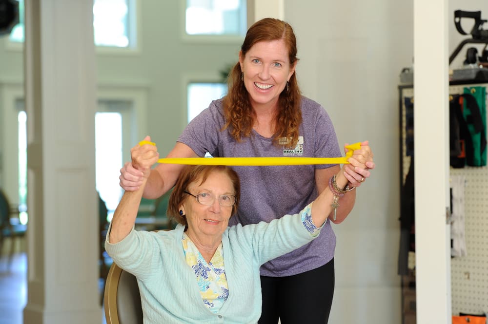 A therapist helps a senior woman exercise with a resistance band.