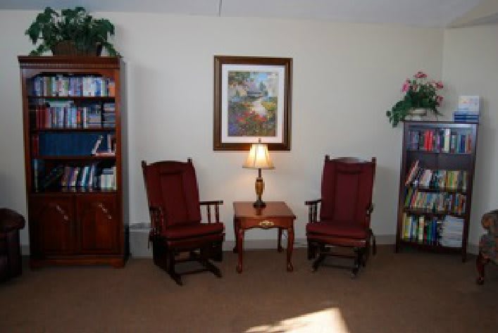 A cozy living room with two rocking chairs, a small table with a lamp, and bookshelves.