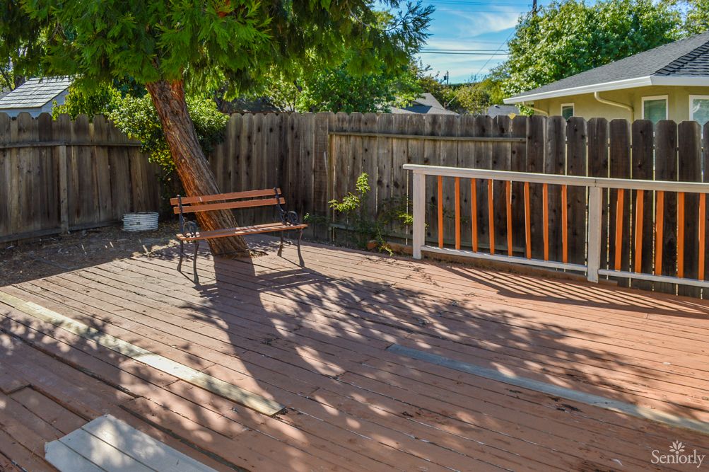 A tranquil backyard deck with a wooden bench and surrounding trees.