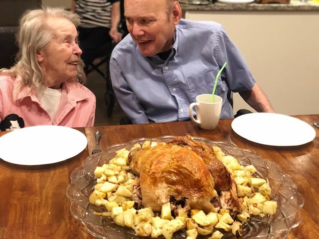 An elderly couple enjoying a meal with a roasted turkey centerpiece.