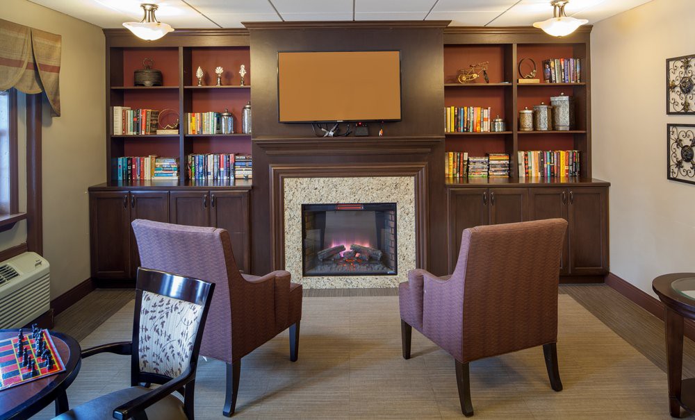 A cozy library setting with a fireplace, surrounded by bookshelves and comfortable armchairs.