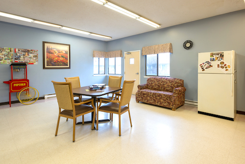 A cozy dining area featuring a table and chairs, a colorful sofa, and large windows that let in natural light.