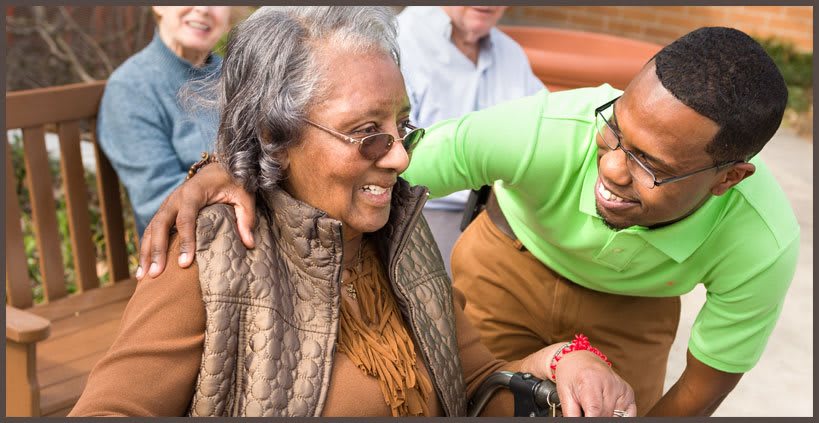 An elderly woman wearing sunglasses is smiling, sharing a warm moment with a friend outdoors.