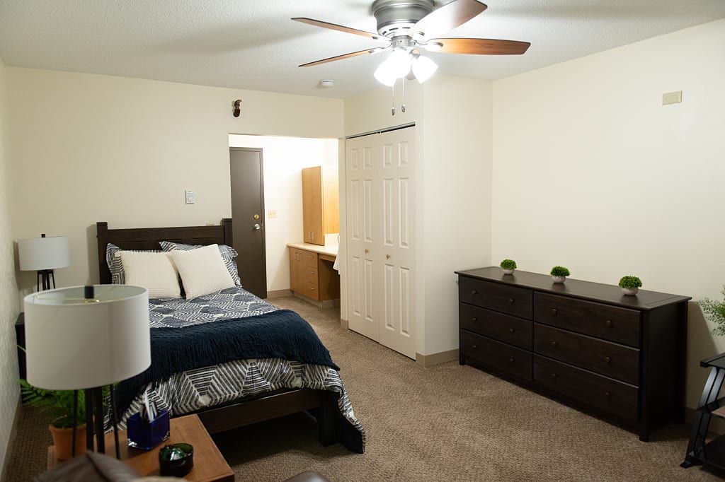 A neatly arranged bedroom with a bed, dresser, and ceiling fan.
