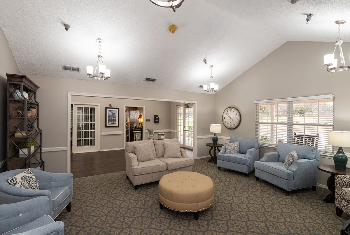 A cozy and well-lit living room with comfortable sofas and chairs arranged around a central ottoman.