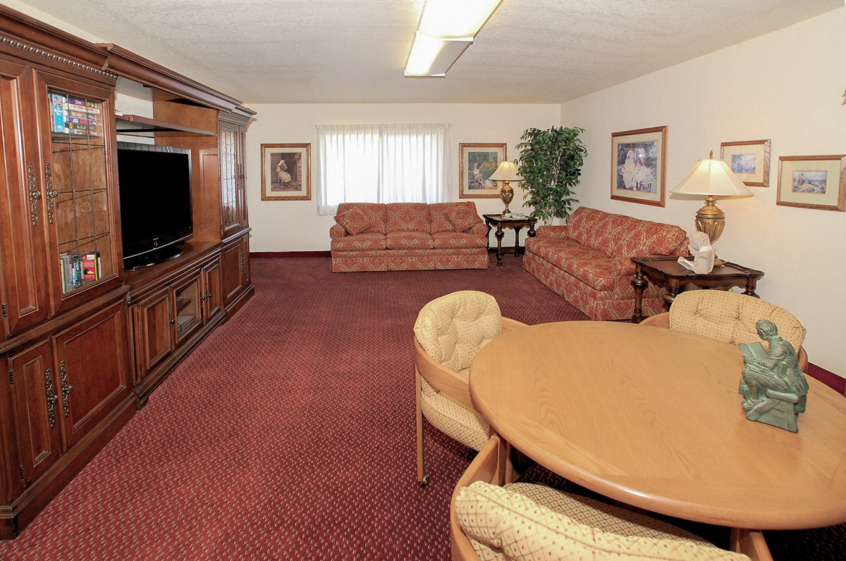 A spacious living room with sofas, a TV, and a round table on a carpeted floor.