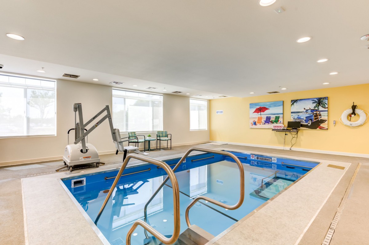 An indoor swimming pool with bright lighting, featuring a pool lift and adjacent seating area, typically found in hotel recreational facilities.