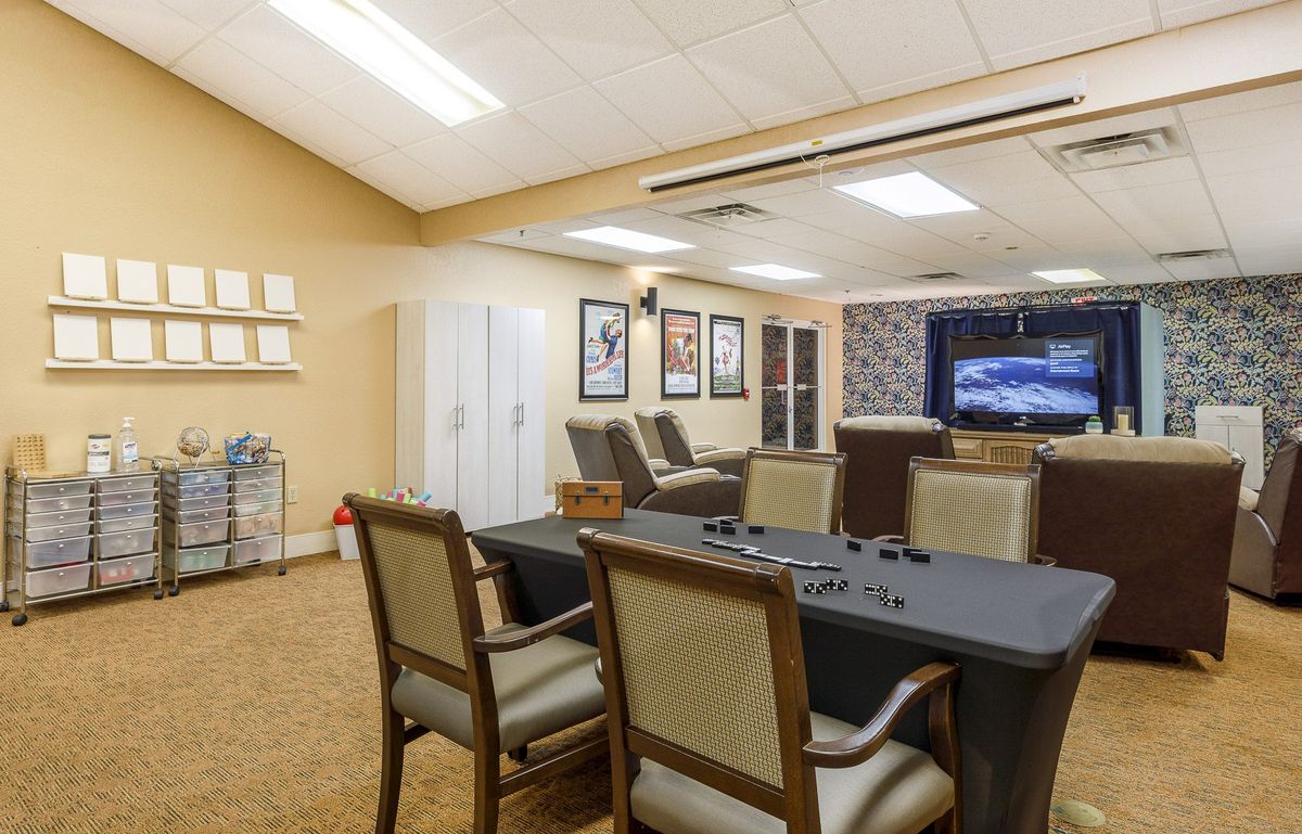 A cozy indoor space featuring a television, several chairs, a table, and decorative posters on the wall.