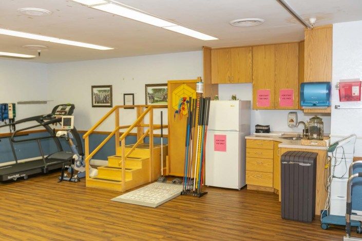 A rehabilitation room equipped with exercise stairs, a kitchen setup, and various therapy tools.