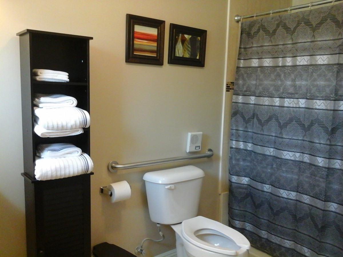 A tidy bathroom with a toilet, shower curtain, and neatly arranged towels on a shelf.