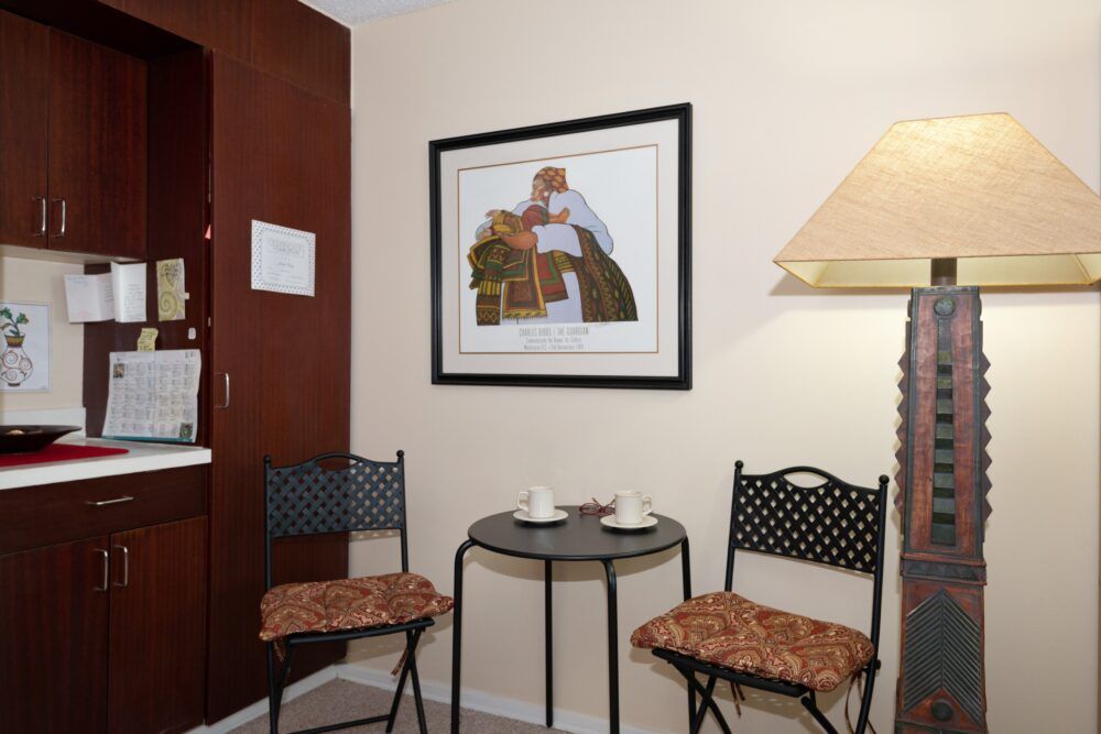 A cozy corner featuring a small round table with two chairs, adorned with artwork and a lamp.