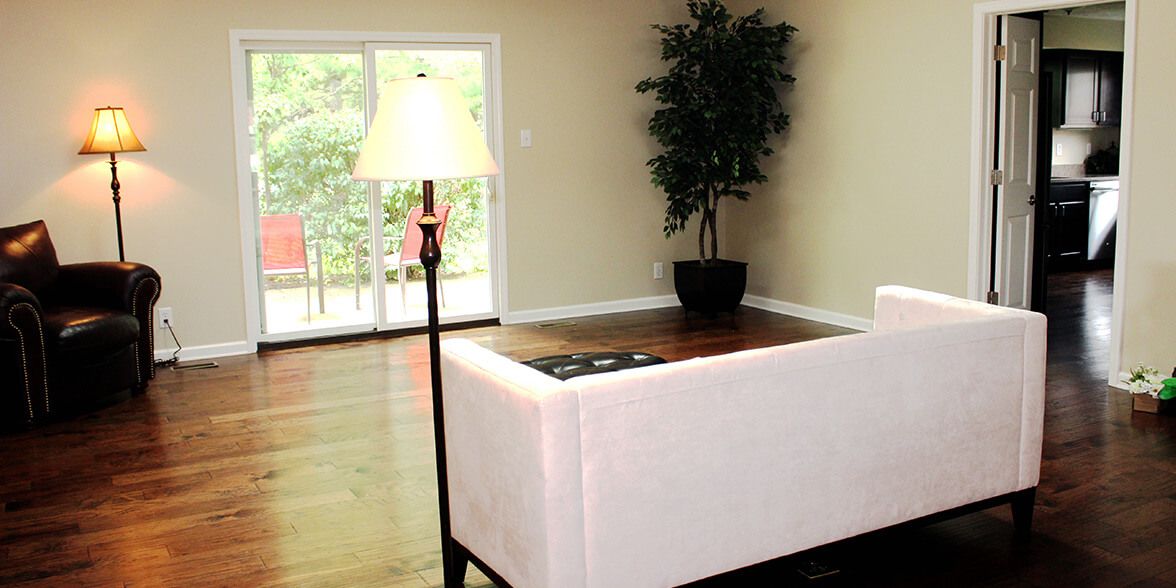 A bright and spacious living room with a sofa, lamp, potted plant, and sliding glass door.