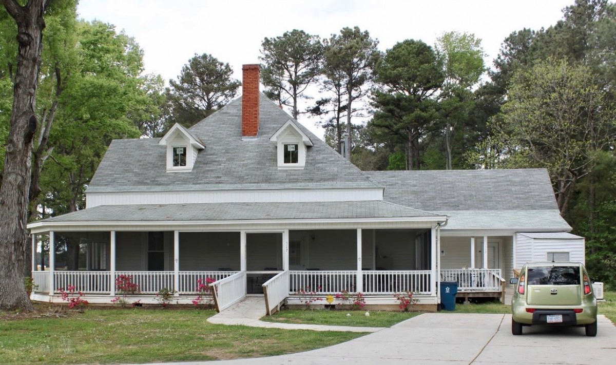 A suburban house with a large porch and a chimney, surrounded by trees.