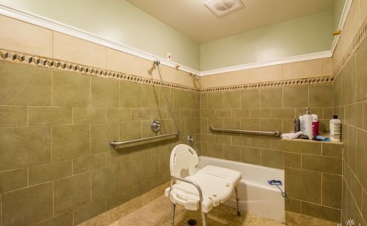 An accessible bathroom equipped with a shower, bathtub, safety grab bars, and a chair for ease of use.