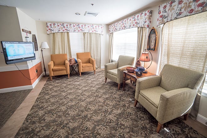 A cozy living room setup with several armchairs, a patterned carpet, and large windows with curtains.