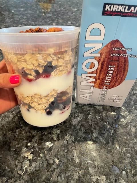 A layered breakfast parfait with yogurt, granola, and mixed berries next to a carton of almond milk.