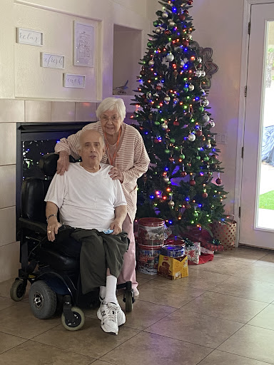 An elderly couple posing together in front of a beautifully decorated Christmas tree.