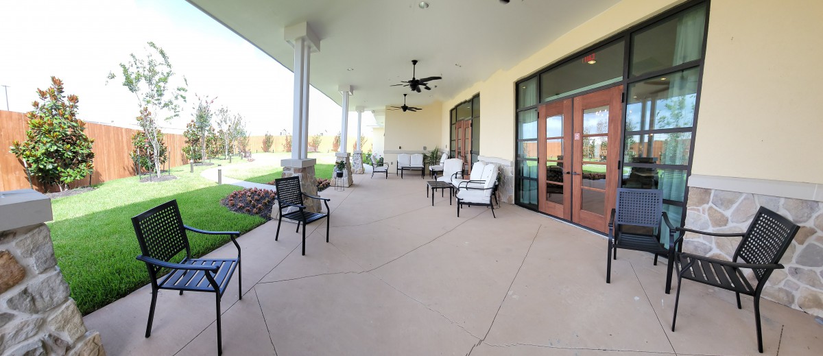 A spacious outdoor patio with comfortable seating and ceiling fans, adjacent to large glass doors.