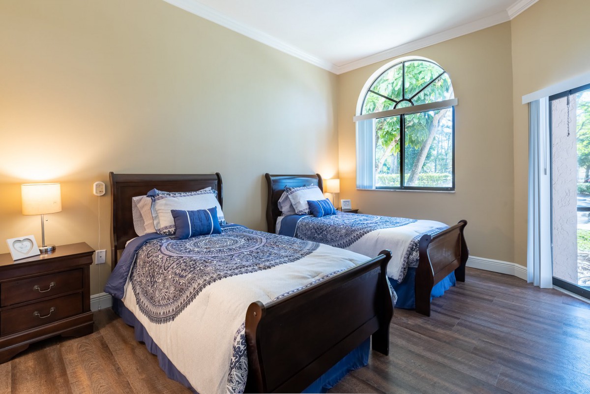 A cozy bedroom with two twin beds featuring blue and white bedding, a large window, and warm lighting.