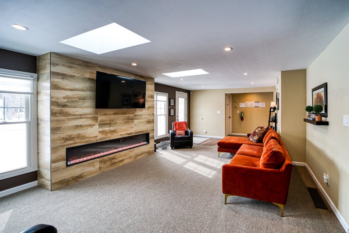 A modern living room with a stylish orange sofa, wall-mounted TV, and a contemporary fireplace.