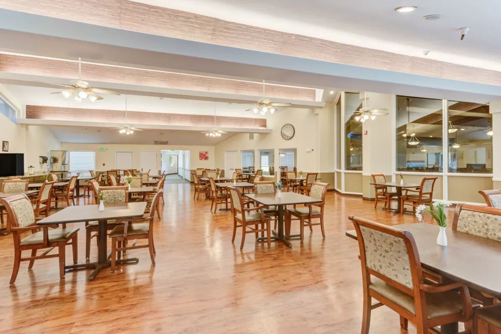 Spacious dining area with wooden tables and chairs, featuring a polished wood floor and soft lighting.