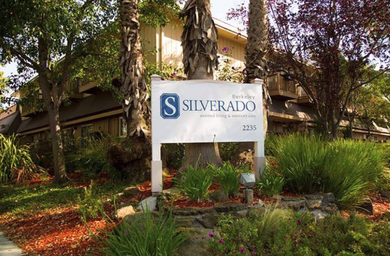 A sign for Silverado surrounded by trees and plants.