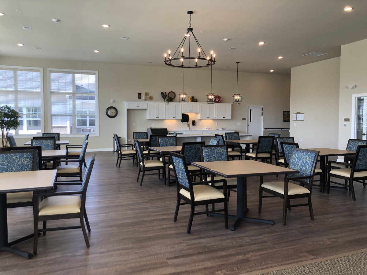A spacious and modern dining area with multiple tables and chairs, featuring a well-lit kitchen.
