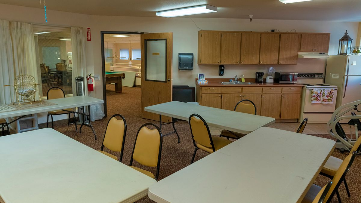 A community room with tables, chairs, and a kitchenette setup.