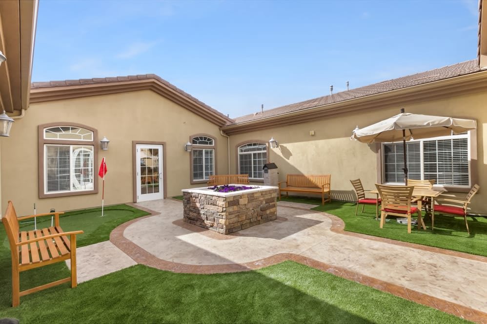 A cozy courtyard featuring a seating area with benches, artificial grass, and a central fountain.