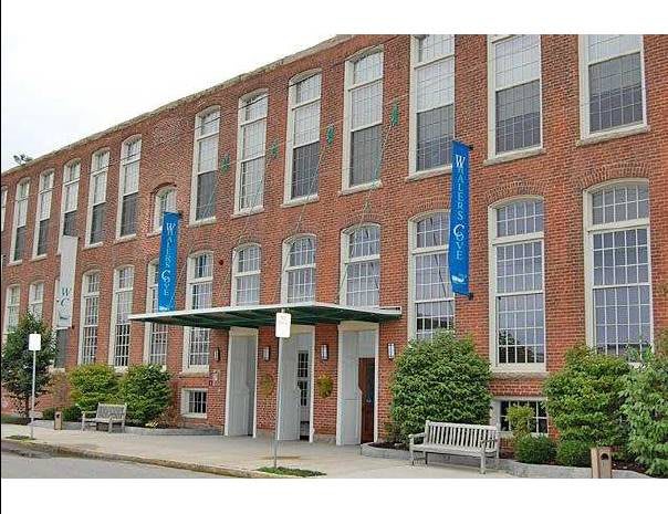 A brick building with large windows and blue banners next to a landscaped entrance.