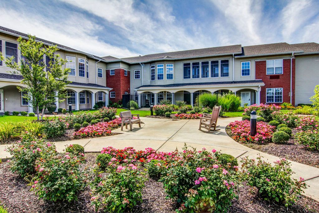 A well-maintained building surrounded by a landscaped garden with benches and colorful flowers under a partly cloudy sky.