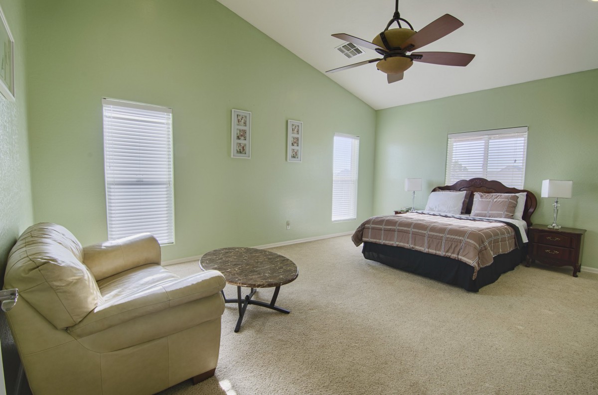 A spacious bedroom with a bed, chair, and ceiling fan.