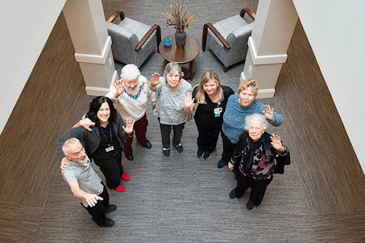 A cheerful group of seniors gathers together in a warm and inviting indoor space, happily waving at the camera.