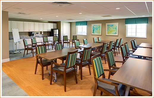A spacious dining area with multiple tables and chairs, featuring a kitchen area in the background.