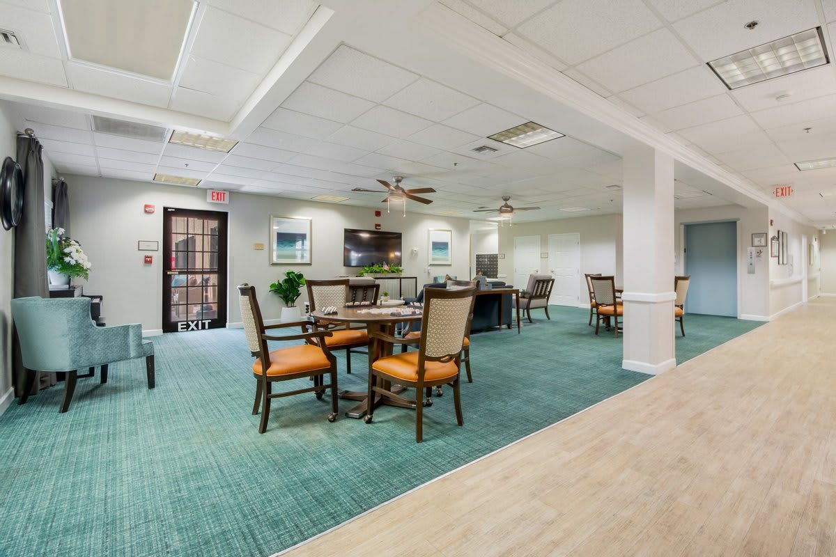 A well-lit dining area with tables and chairs, featuring ceiling fans and a green carpet.