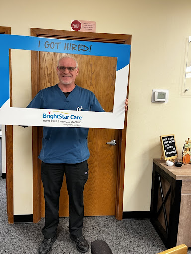 A cheerful man posing with a Brightstar Care frame in an office setting.